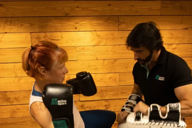 Boxing Camp Muay Thaï à Active Square Pessac : une adhérente frappe dans les paos tenus par le coach Bertrand